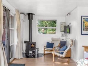 Une pièce chaleureuse avec un poêle à bois, une fenêtre donnant sur la verdure et un fauteuil confortable agrémenté de coussins.