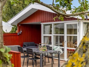 A covered outdoor patio with a table and chairs, a red building in the background, and a glass door leading to a dining area. - "Laurine" - 500m from the sea by Interhome (Sydals)