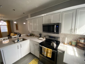 A modern kitchen with white cabinets, a stainless steel microwave, a stove, and a sink. - Charming apartment with AC in vibrant Nassau perfect for couples, relaxing. (Nassau)