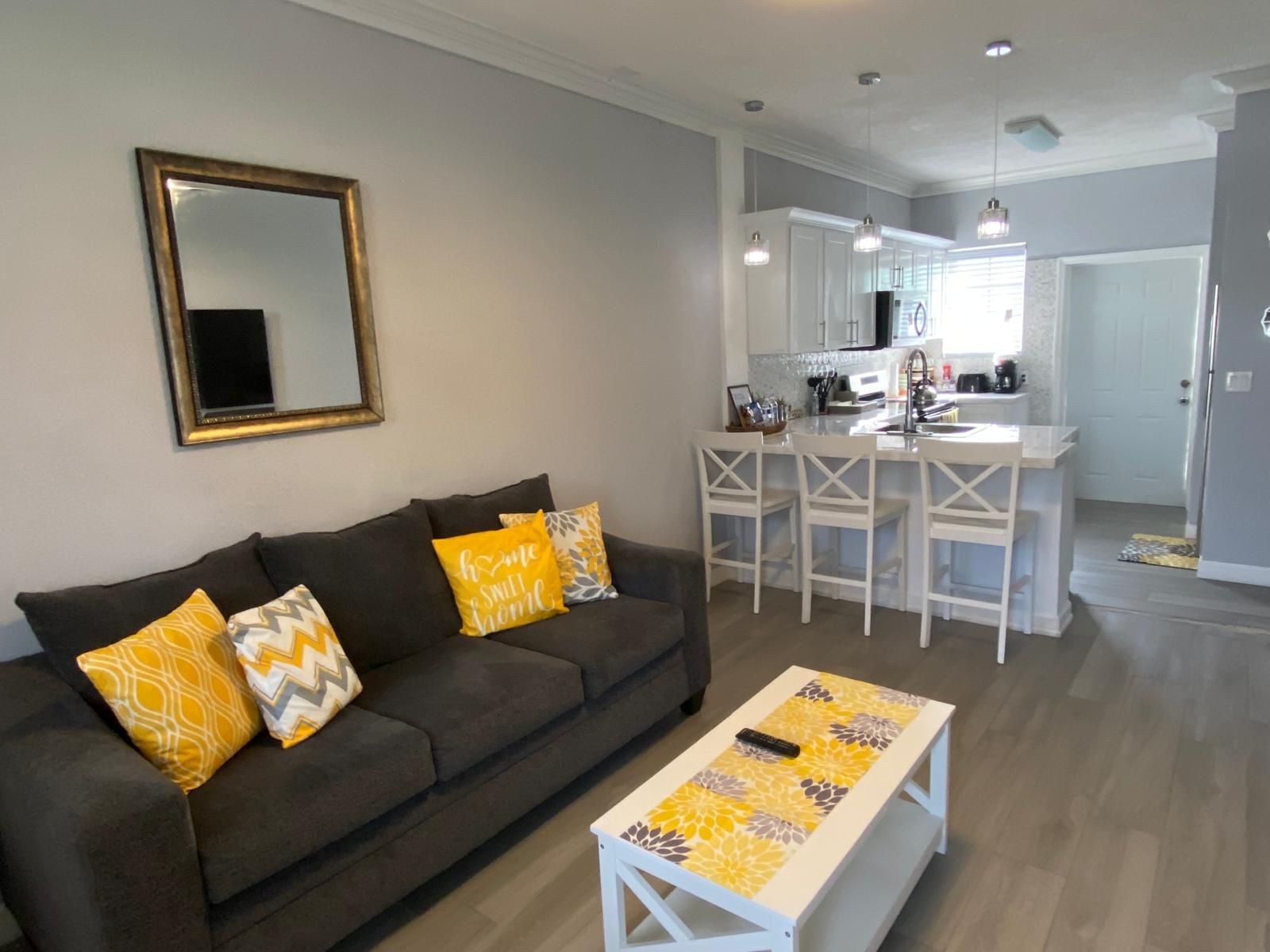 A living room with a sofa, a coffee table, and a kitchen area with a counter and chairs.