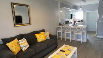 A living room with a sofa, a coffee table, and a kitchen area with a counter and chairs.