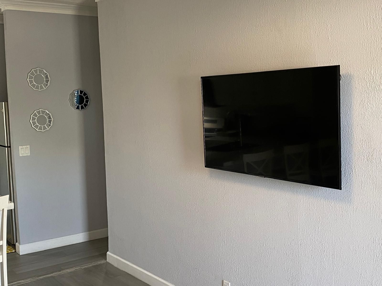 A room with a flat-screen TV mounted on the wall, a door with a circular mirror, and a light switch.