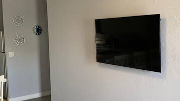 A room with a flat-screen TV mounted on the wall, a door with a circular mirror, and a light switch.