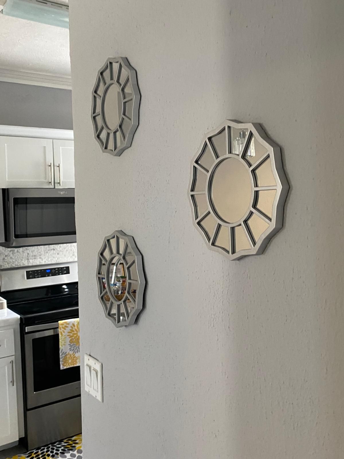 A kitchen with white cabinets, a microwave, and a stove. There are three wall clocks with different designs.