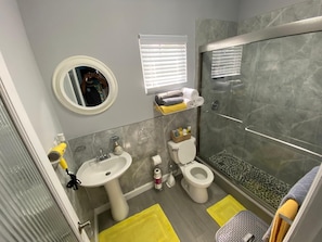 A bathroom with a sink, toilet, and shower. There is a mirror, a window with blinds, and a shelf with towels. - Charming apartment with AC in vibrant Nassau perfect for couples, relaxing. (Nassau)