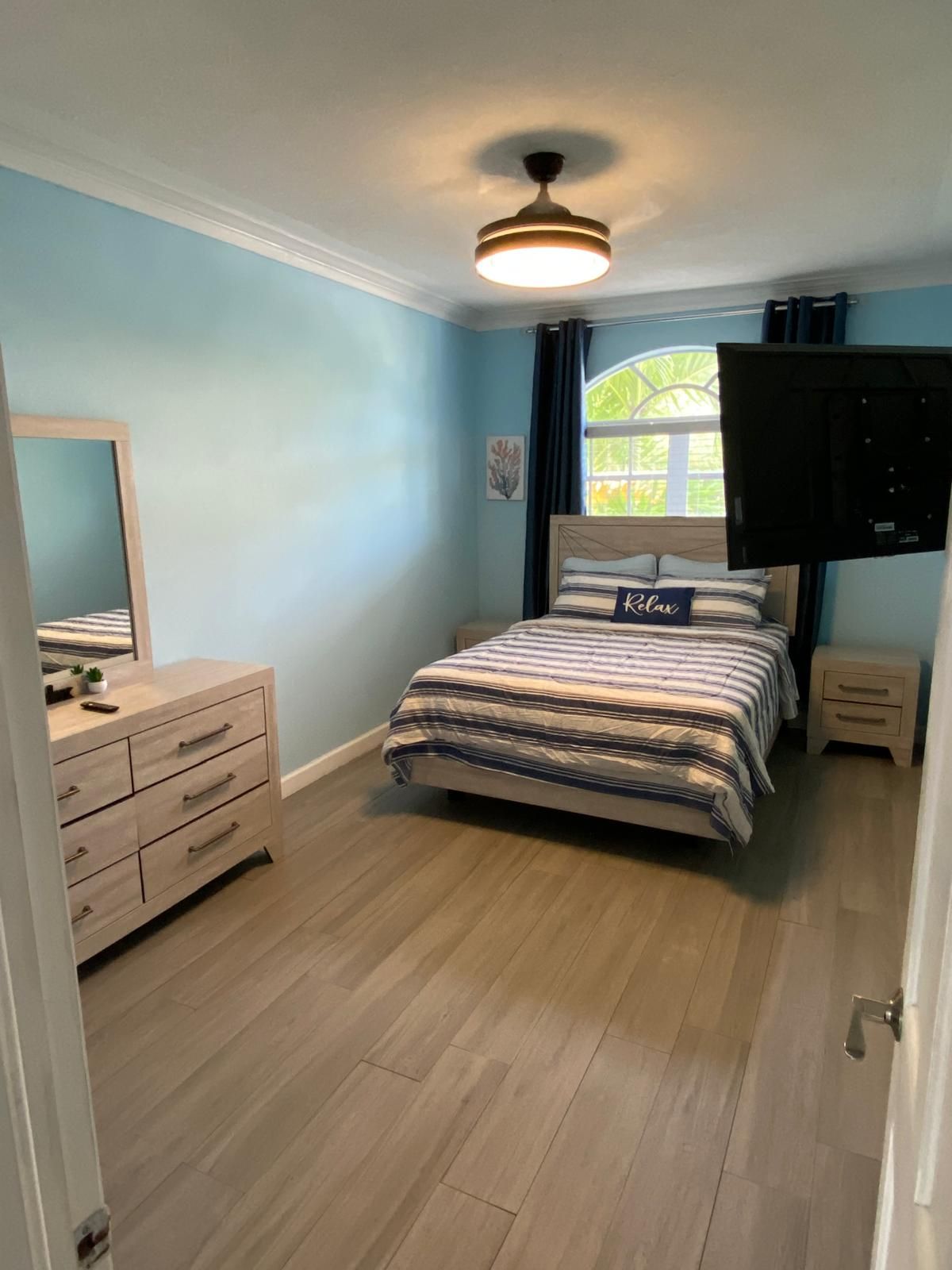 A bedroom with a bed, a dresser, a mirror, and a ceiling fan.