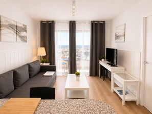 A modern living room with a sofa, a coffee table, a TV, and a view of the city through large windows. - Ocean House Apartment Sea View Block 3, 7th Floor (Torremolinos)