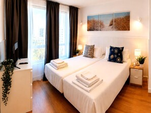 Ein Hotelzimmer mit zwei Betten, einem Schreibtisch, einem Stuhl, einer Topfpflanze und einem Bild an der Wand.