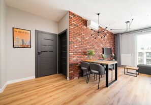 A modern living room with a brick accent wall, a dining area with a wooden table and chairs, and a large window providing a view of the city. - Mokotów Residence Apartment (Warszawa)
