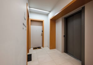 A hallway with a door, a doormat, and a wall-mounted elevator control panel. - Mokotów Residence Apartment (Warszawa)