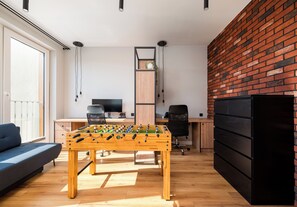 A modern living space with a foosball table, a blue sofa, a wooden desk, a computer, and a brick wall. - Mokotów Residence Apartment (Warszawa)