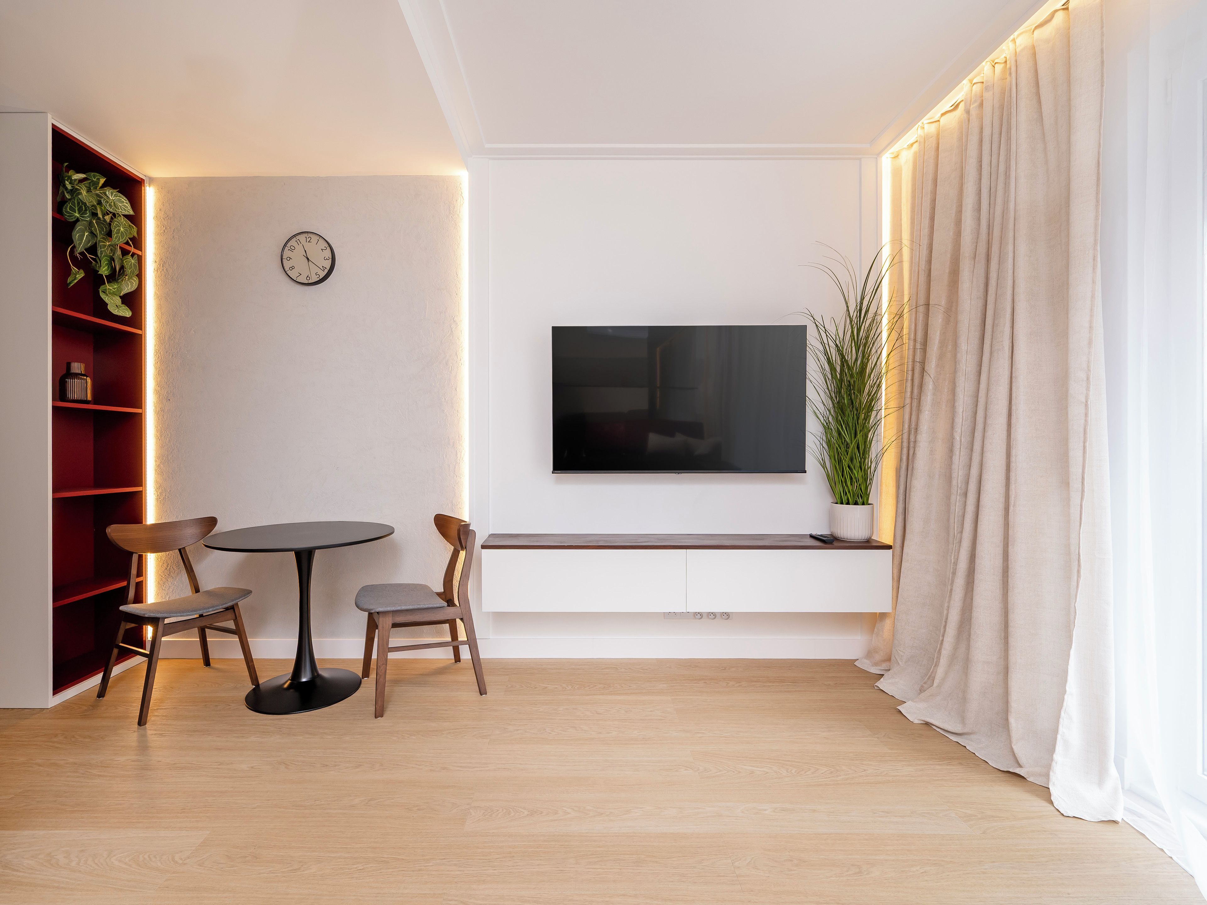 A modern living room with a flat-screen TV, wooden furniture, a clock, and a plant.