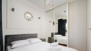 A modern hotel room with a large bed, a mirror, and decorative wall sconces. - Wola Grzybowska Lavish Apartment (Warszawa)