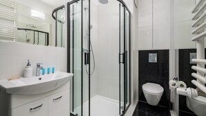 A modern bathroom with a glass-enclosed shower, a white sink with toiletries, and a toilet with a paper towel dispenser. - Wola Grzybowska Lavish Apartment (Warszawa)