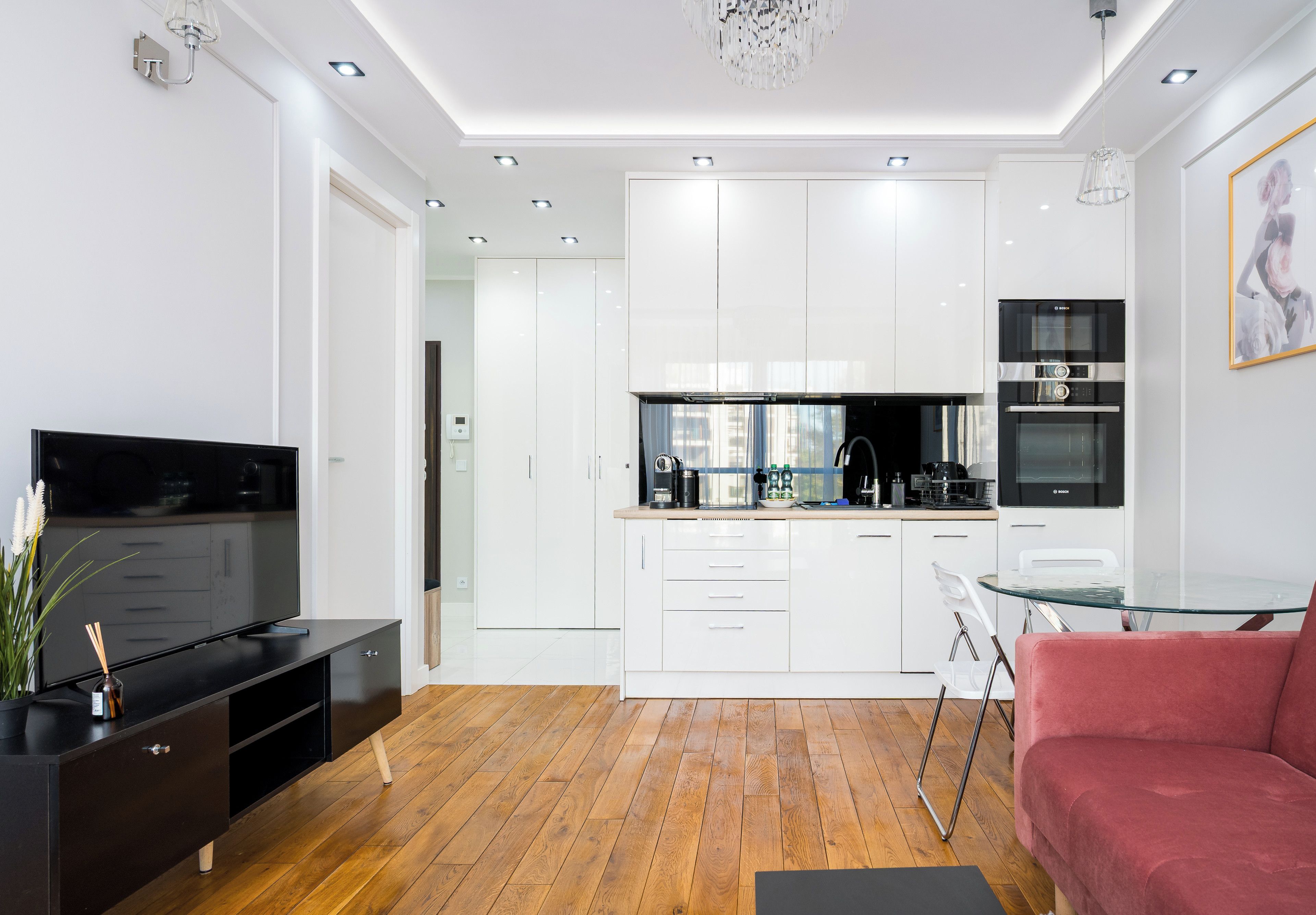 A modern kitchen with white cabinets, a Bosch oven, and a glass coffee table.