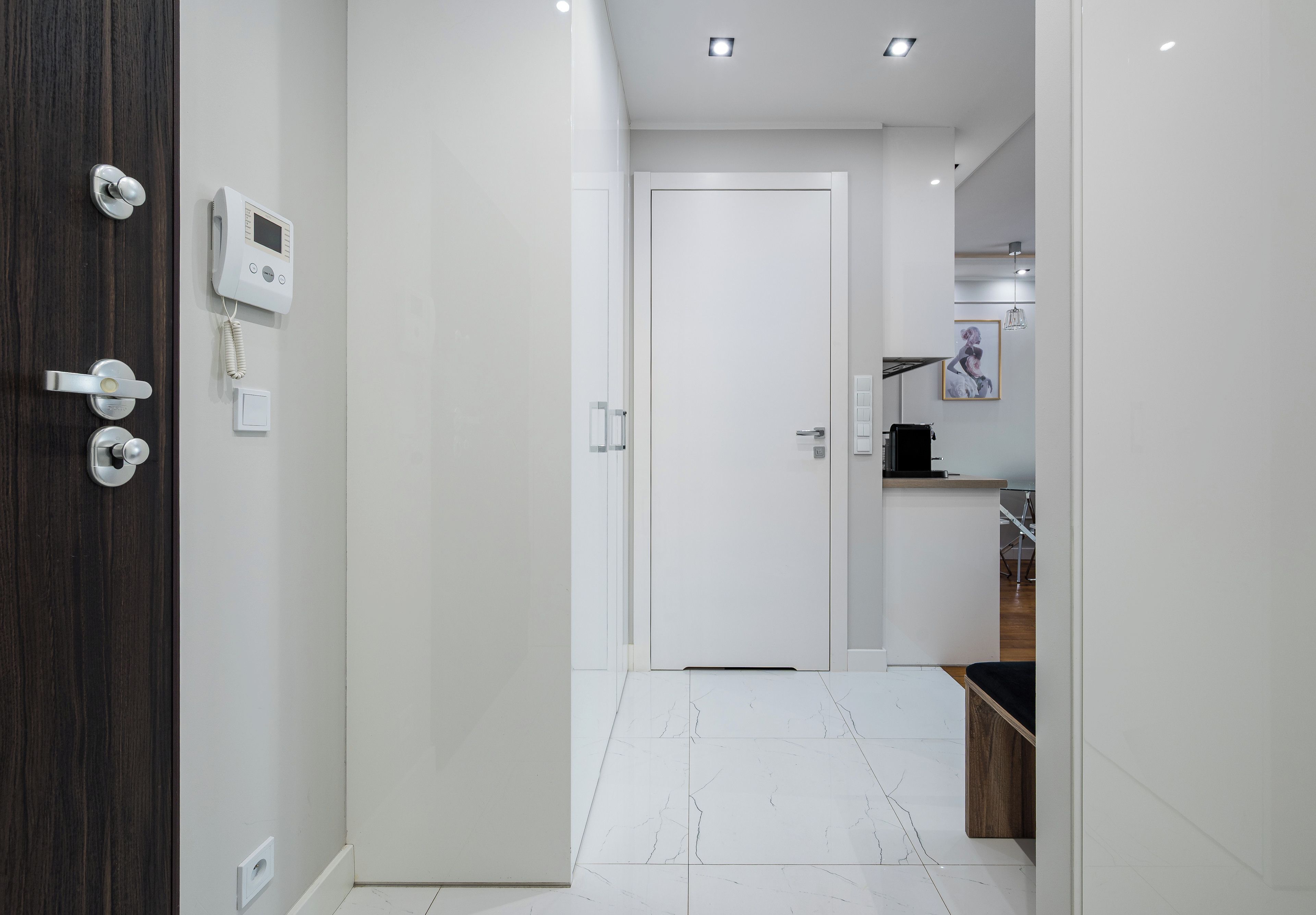 A modern hallway with a white door, a digital thermostat, and a light switch on the wall.