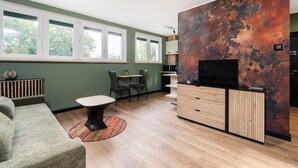 Una sala de estar moderna con sofá, mesa de centro, televisor y zona de cocina con armarios y encimera.