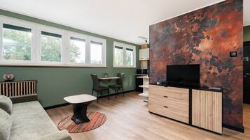 A modern living room with a sofa, a coffee table, a TV, and a kitchen area with cabinets and a countertop.