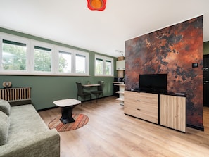 Uma sala de estar moderna com sofá, mesa de centro, televisão e área de cozinha com armários e bancada.