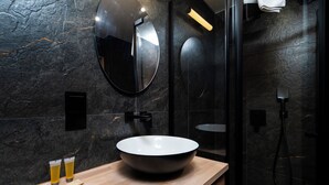 Un baño moderno con un lavamanos ovalado grande, un espejo redondo y una ducha con cerramiento de vidrio.