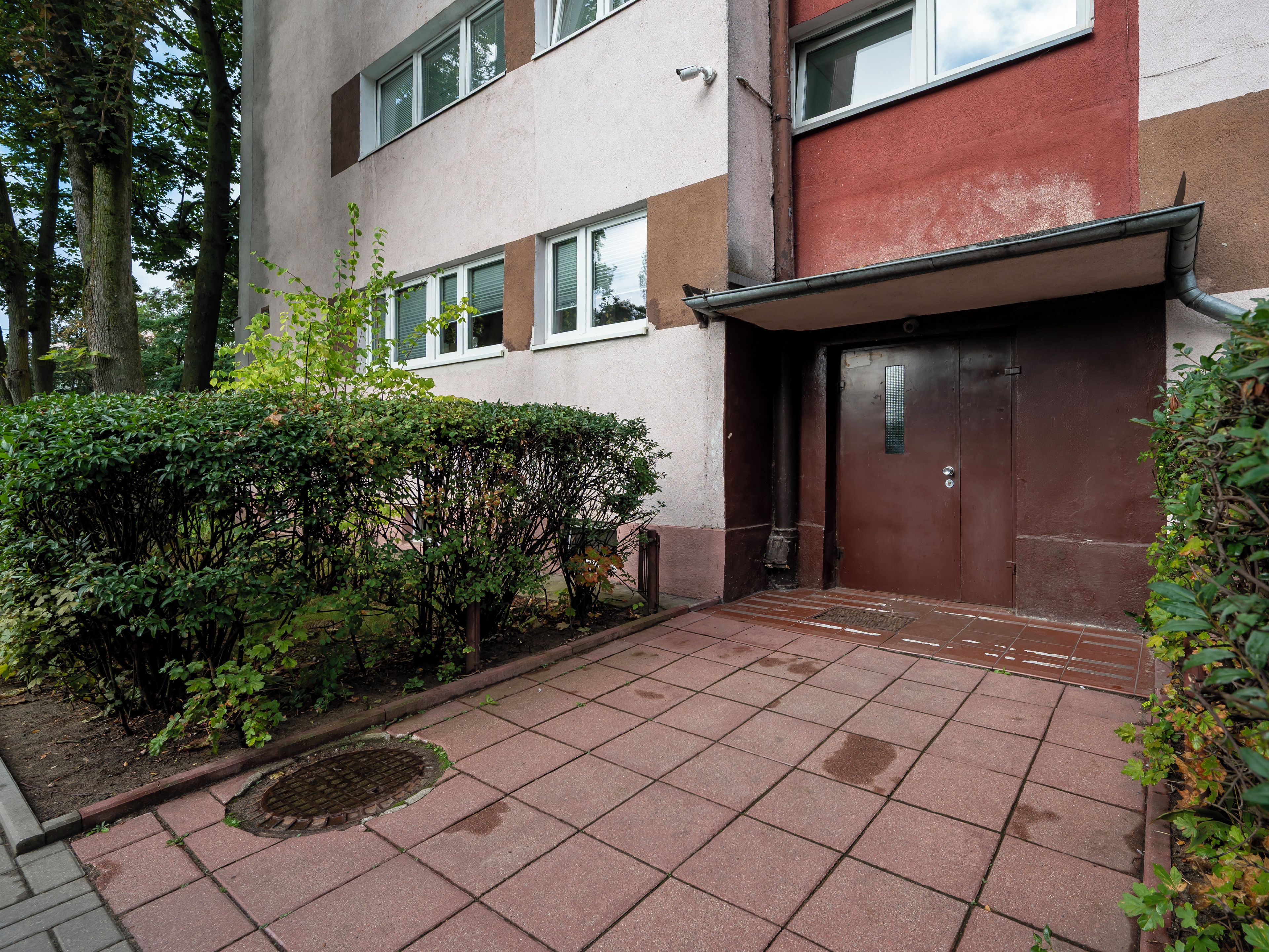 A building with a brown door, a small entrance, and a tiled patio area.
