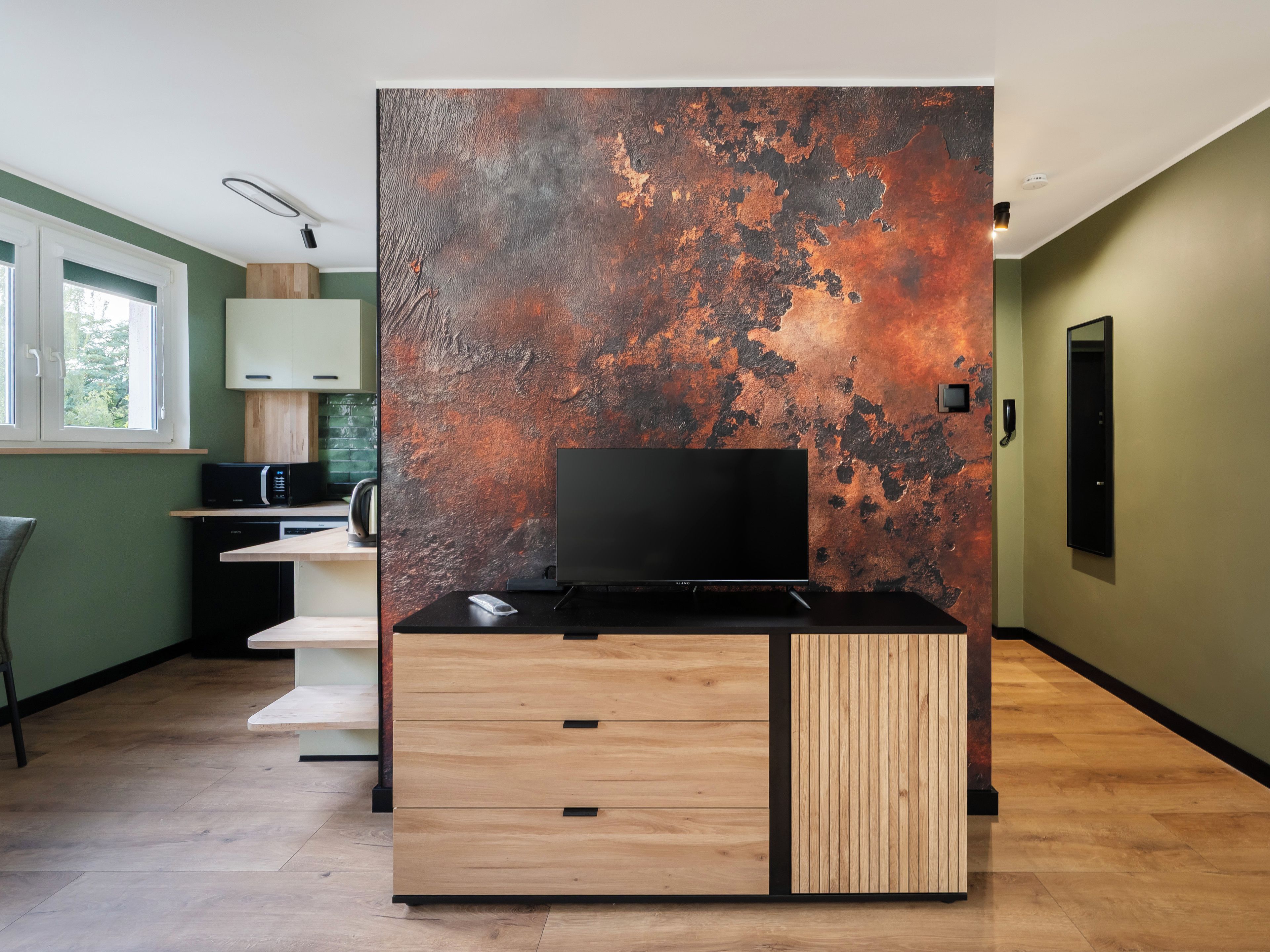 A modern kitchen with a flat-screen TV, wooden cabinetry, and a rustic wall.