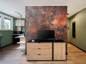 A modern kitchen with a flat-screen TV, wooden cabinetry, and a rustic wall. - Aleksandrowska City Prestige Studio (Łódź)