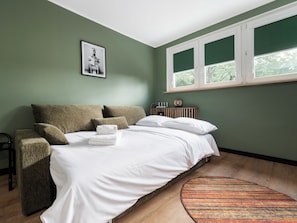Quarto com cama, travesseiros, uma cadeira, mesa de cabeceira, um quadro emoldurado e uma janela.