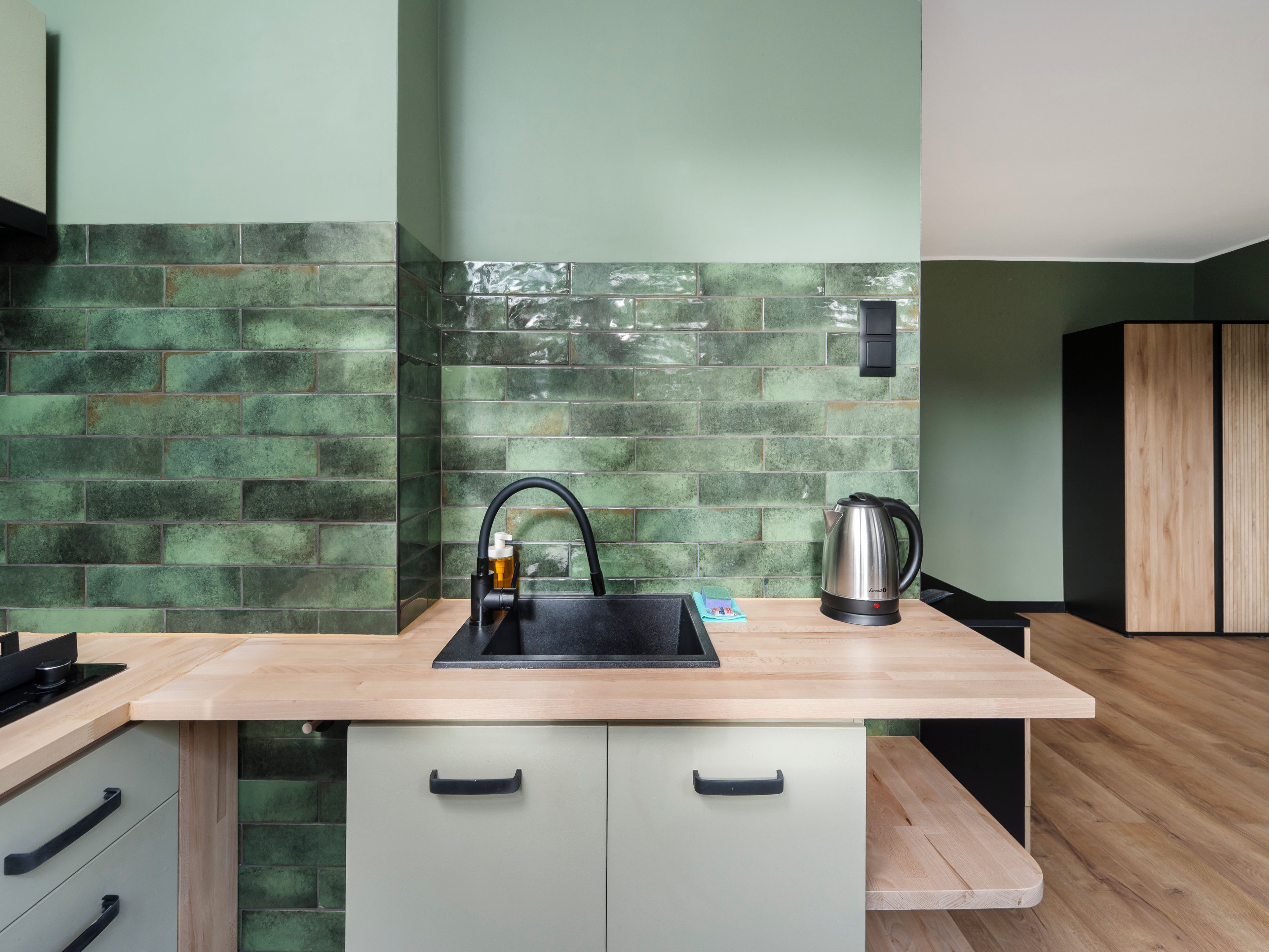 A kitchen with a modern design, featuring a sink, a kettle, and a wooden countertop.
