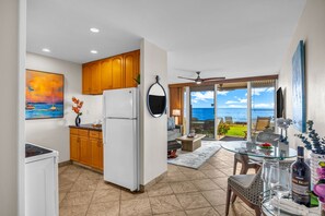 A modern kitchen with wooden cabinets, a white refrigerator, and a dining area with a glass table and chairs. - Oceanfront Lahaina Oasis 1 Bedroom (Lahaina)