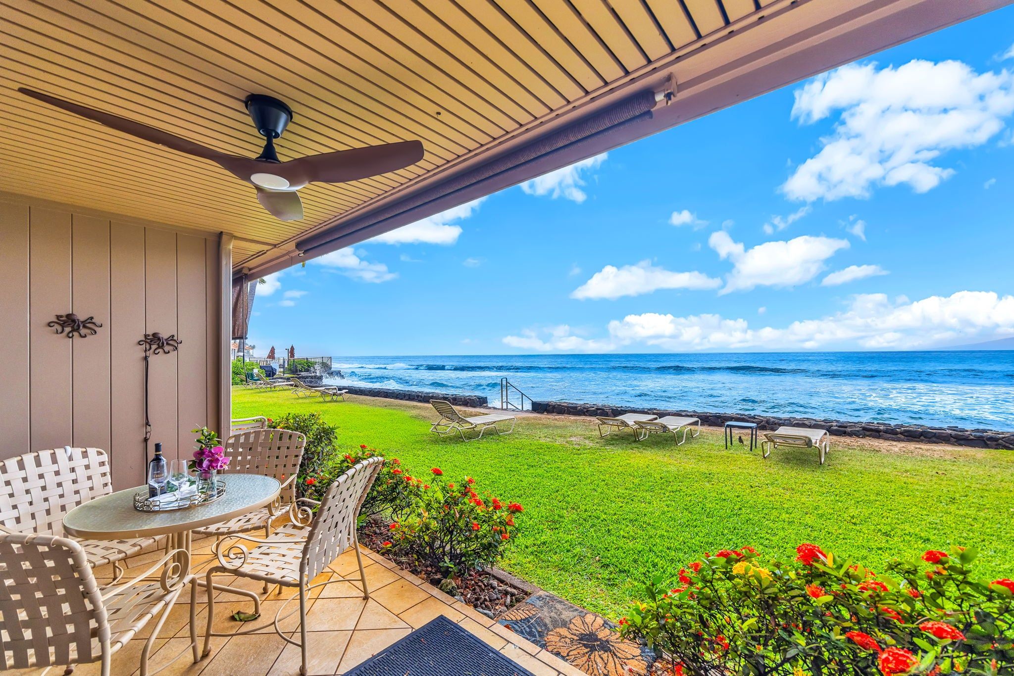 A covered patio with a table and chairs, overlooking the ocean.
