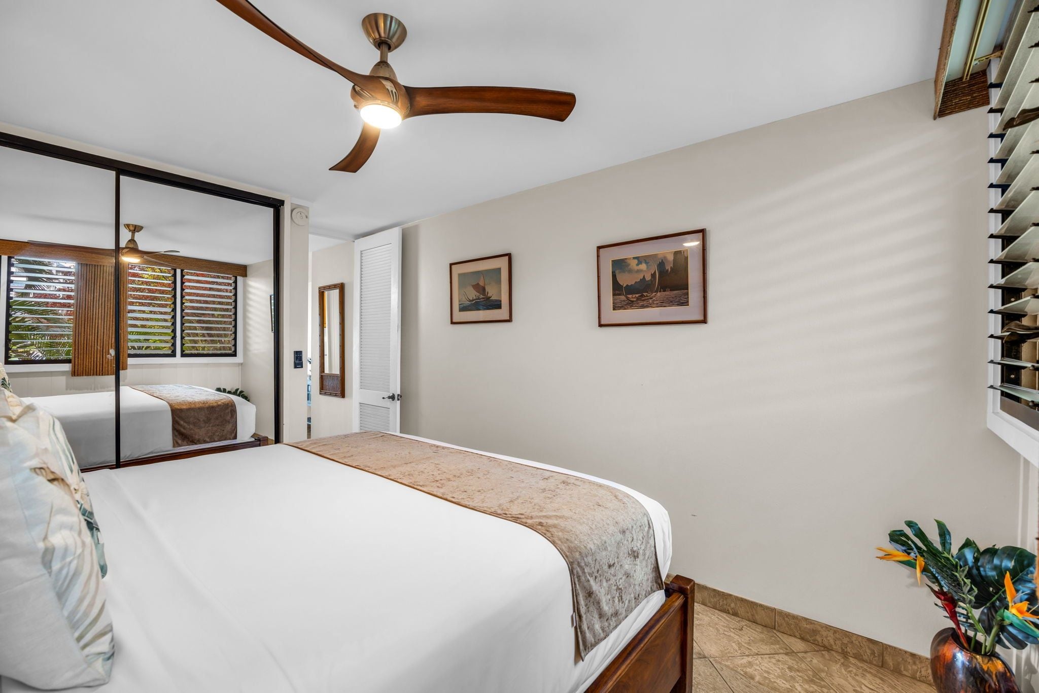 A bedroom with a bed, a ceiling fan, a window with blinds, and two framed pictures on the wall.