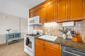 A modern kitchen with wooden cabinets, a white stove, granite countertop, and a built-in dishwasher. - Oceanfront Lahaina Oasis 1 Bedroom (Lahaina)