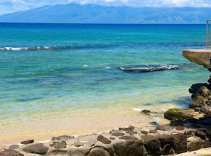 A beach with clear turquoise water, a rocky shoreline, and a distant mountain range. - Oceanfront Lahaina Oasis 1 Bedroom (Lahaina)