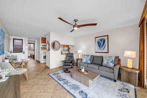 A spacious living room with a ceiling fan, a gray sofa with patterned cushions, a black leather chair, and a coffee table. - Oceanfront Lahaina Oasis 1 Bedroom (Lahaina)