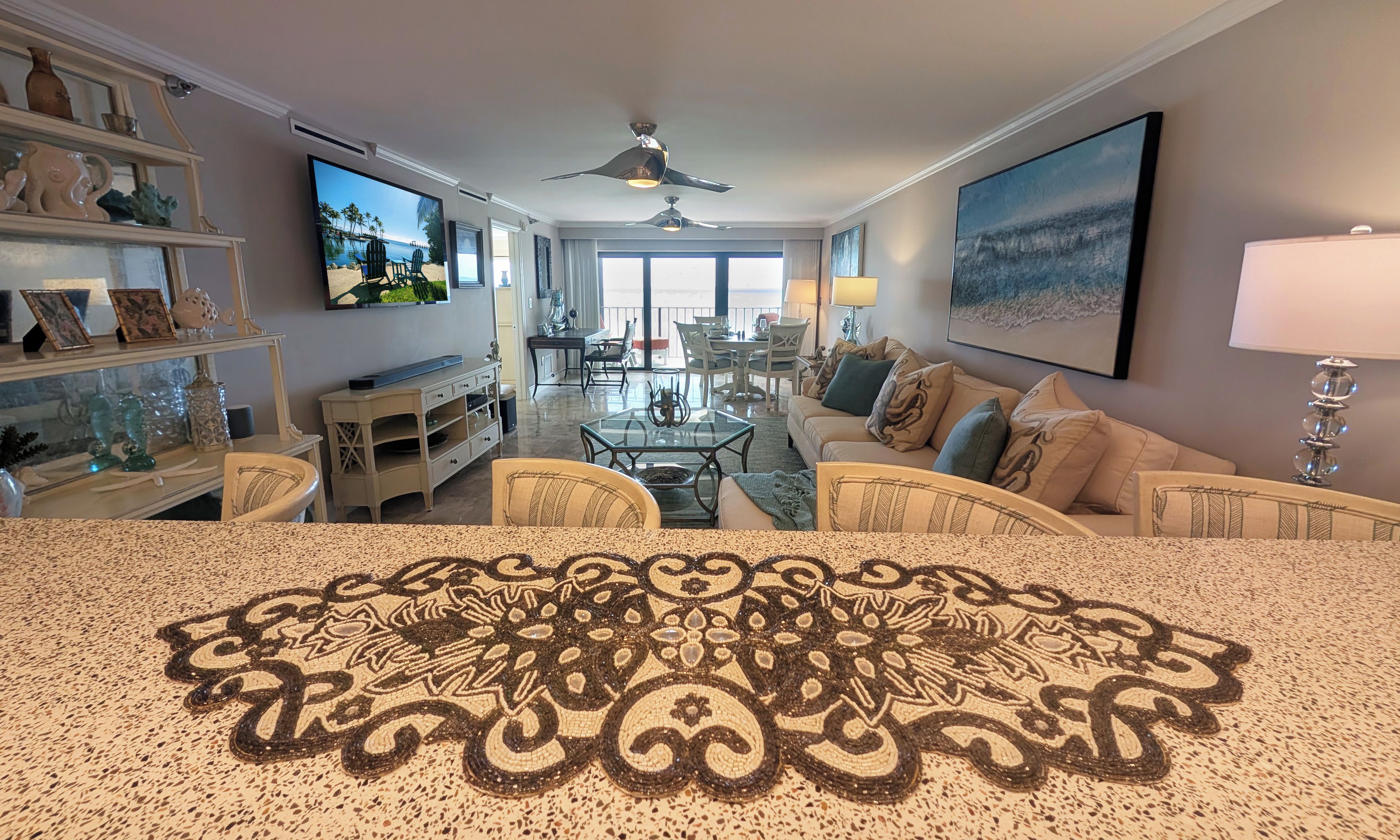 A spacious living room with a large TV, comfortable seating, a ceiling fan, and a view to the outdoors.