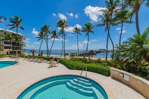 A resort pool area with a view of the ocean, palm trees, and a thatched-roof structure. - Ocean-front 2BR condo in Islamorada with pool, hot tub, gym, and balcony. (Islamorada)