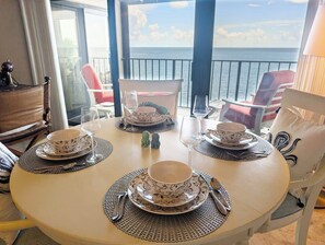 Ein runder Esstisch mit Tellern, Schüsseln und Besteck, mit Blick auf einen Balkon und das Meer.