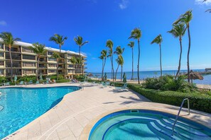 Ein Poolbereich eines Resorts mit freiem Blick auf das Meer, einem mehrstöckigen Gebäude und Palmen.