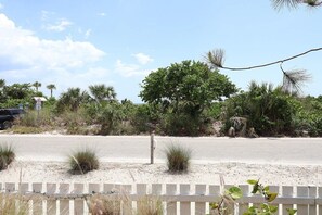 Una playa arenosa con una cerca blanca, palmeras y cielo despejado.