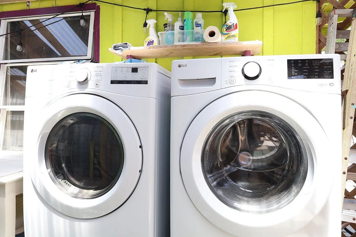 Two front-loading LG washing machines with a shelf above containing cleaning supplies.