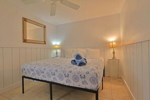 A bedroom with a bed, a ceiling fan, a mirror, and two bedside lamps. - Beach Tree Cottage,Walk To Beach& Siesta (Siesta Key)