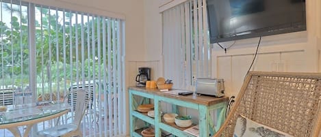Un coin repas comprenant une table, des chaises, une machine à café et un téléviseur fixé au mur.