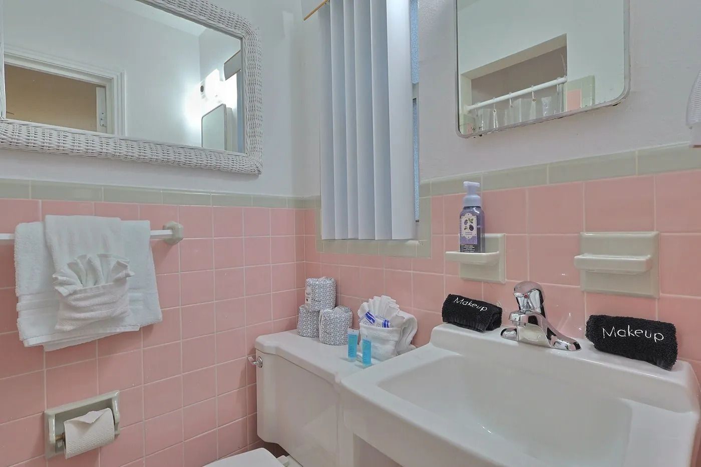 Un bagno con un lavandino bianco, due specchi, un water e piastrelle rosa.