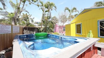 A hot tub with a green inflatable seat, surrounded by a wooden deck and a yellow building.