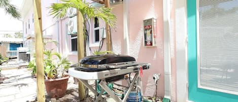 Un patio con una parrilla, plantas en macetas y un edificio con una puerta azul turquesa.