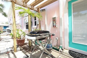 A patio area with a grill, potted plants, and a building with a teal door. - Beach Tree Cottage,Walk To Beach& Siesta (Siesta Key)