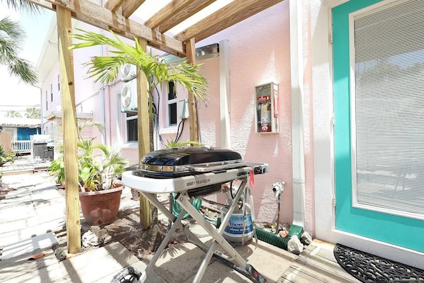 A patio area with a grill, potted plants, and a building with a teal door. - Beach Tree Cottage,Walk To Beach& Siesta (Siesta Key)