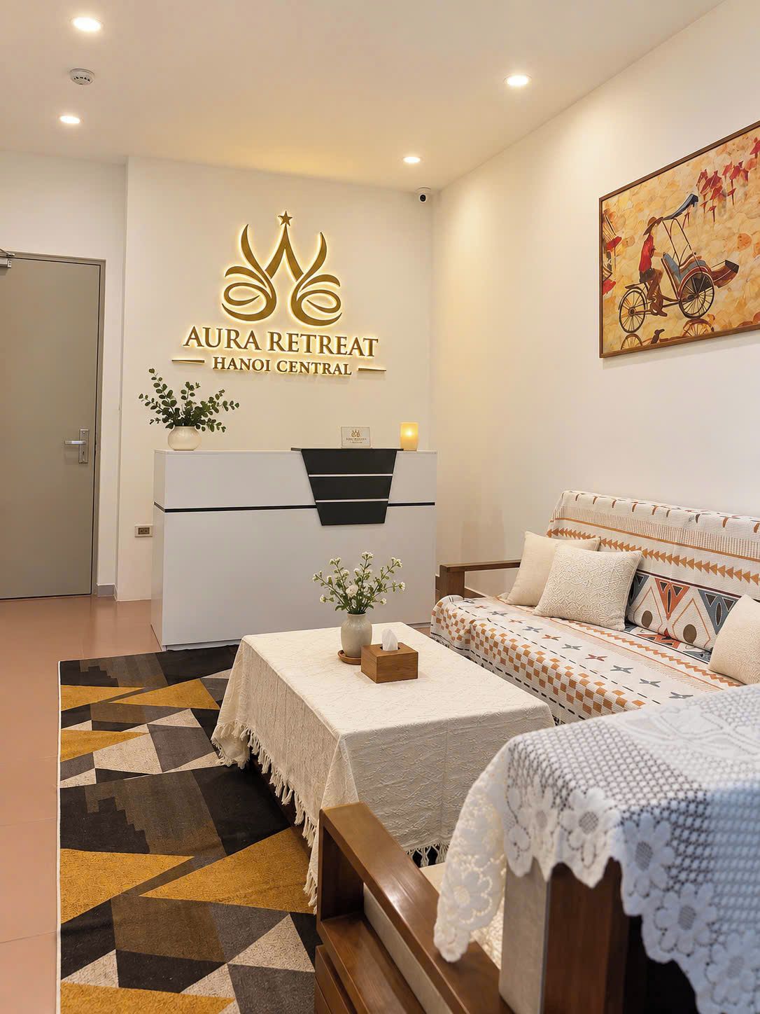 A hotel room with a bed, a desk, a reception desk, and a wall-mounted sign.
