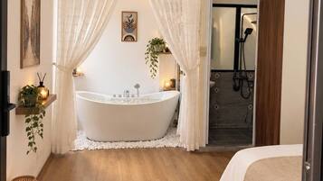 A modern bathroom with a freestanding bathtub, a shower area, and a bed with a woven rug.